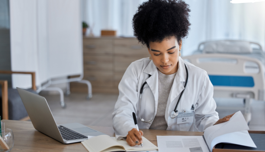 This is a doctor looking at paper and taking notes with a laptop.