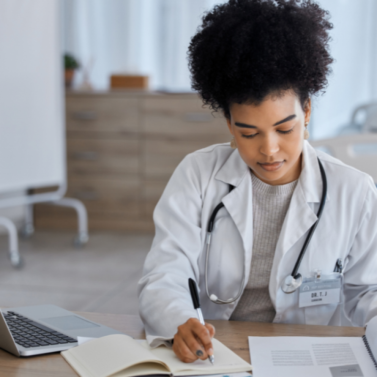 This is a doctor looking at paper and taking notes with a laptop.